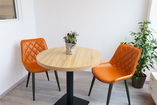 Moderner Essbereich mit rundem Holztisch, zwei orange Stühlen und Zimmerpflanze.