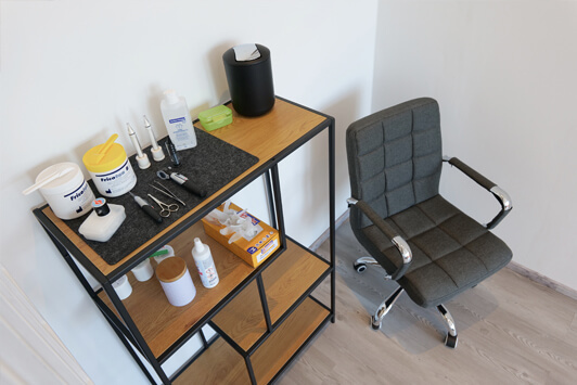 Moderner Behandlungsraum mit grauem Stuhl und Regal voller Kosmetik- und Hygieneprodukte.